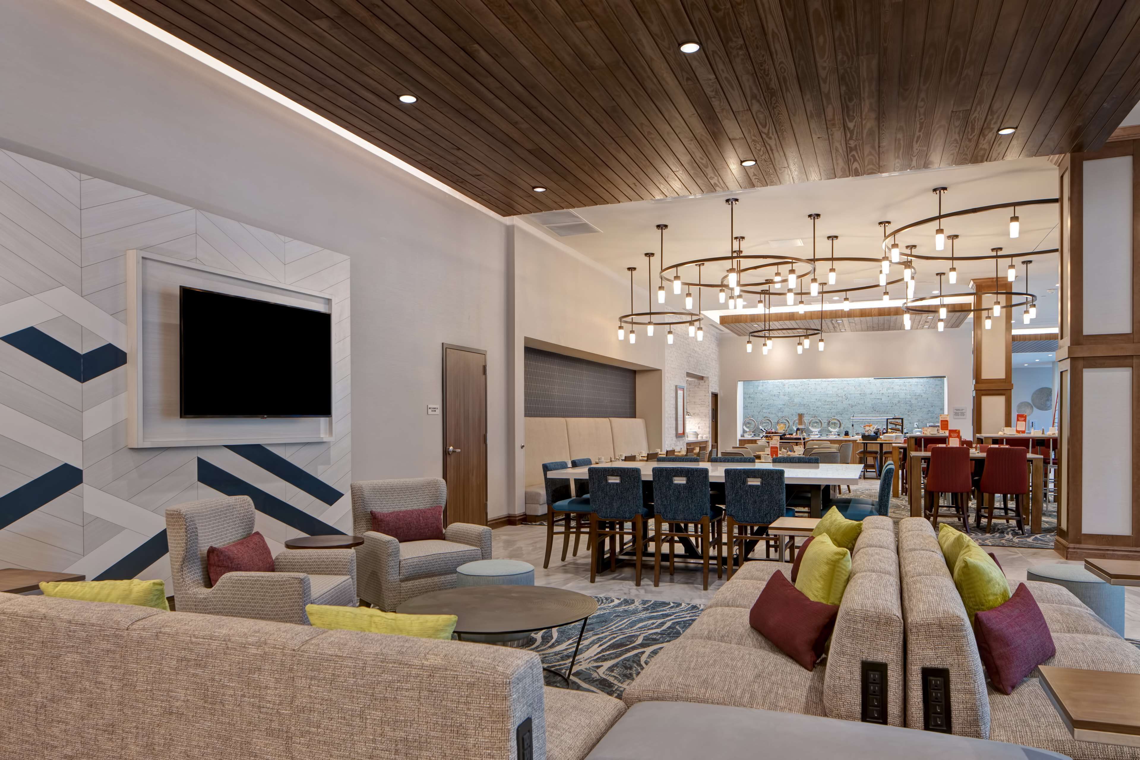 A modern hotel lobby with a large seating area, a dining space, and a bar.