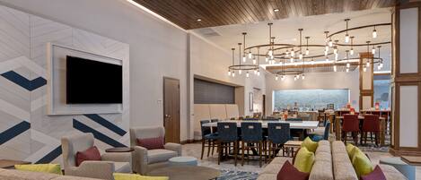 A modern hotel lobby with a large seating area, a dining space, and a bar.