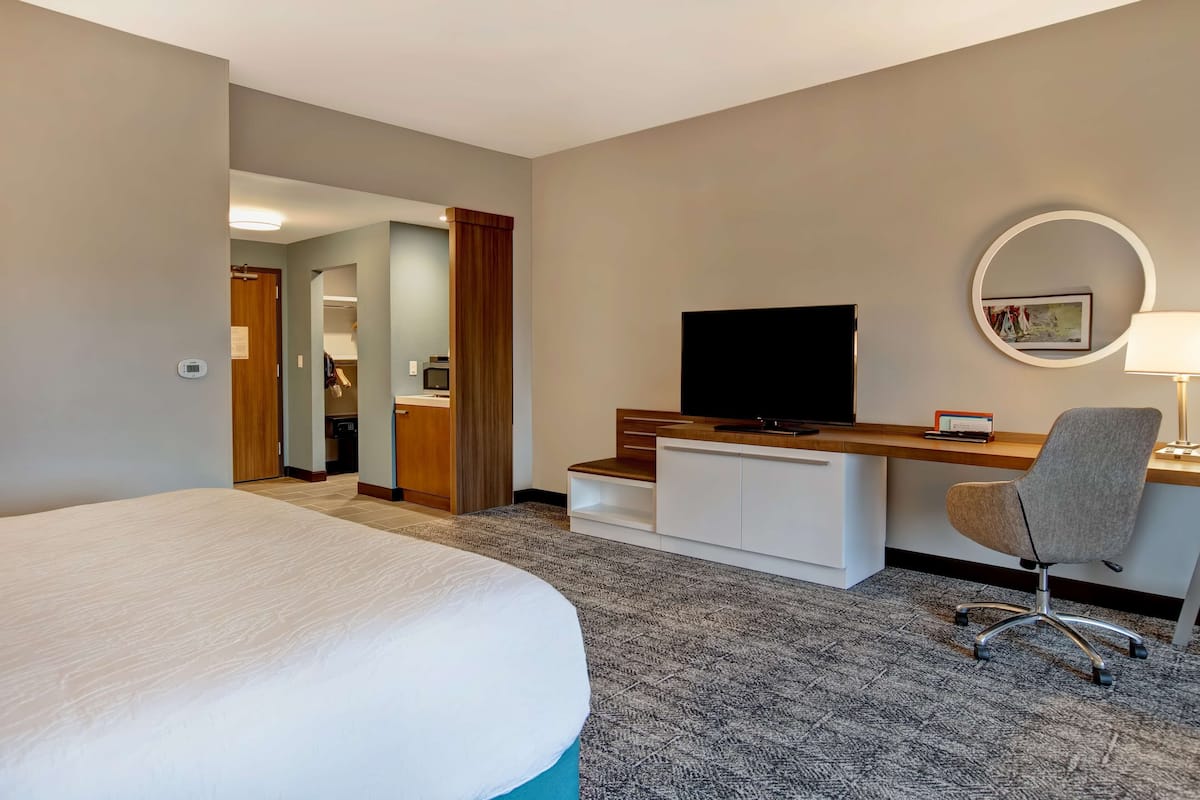A hotel room with a large bed, a desk with a chair, a television, and a small desk lamp.