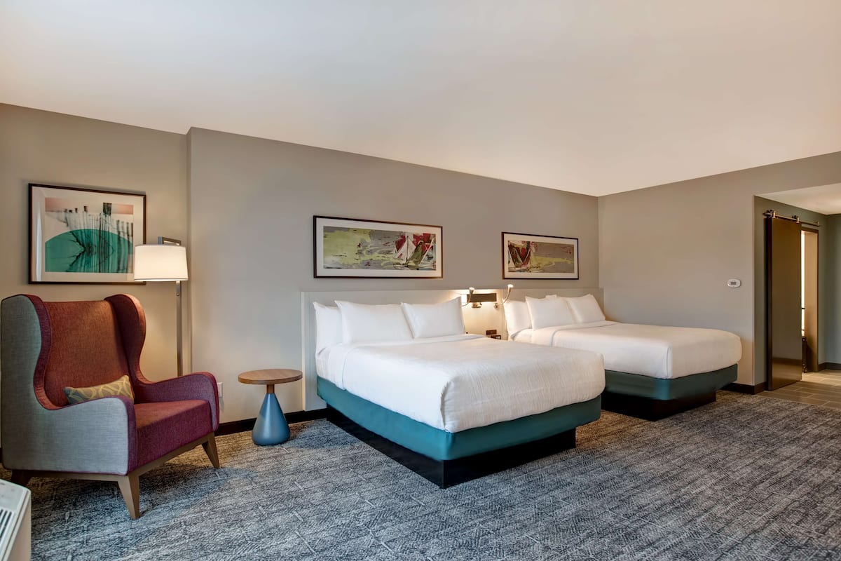 A hotel room with two beds, a red armchair, and two wall-mounted lamps.
