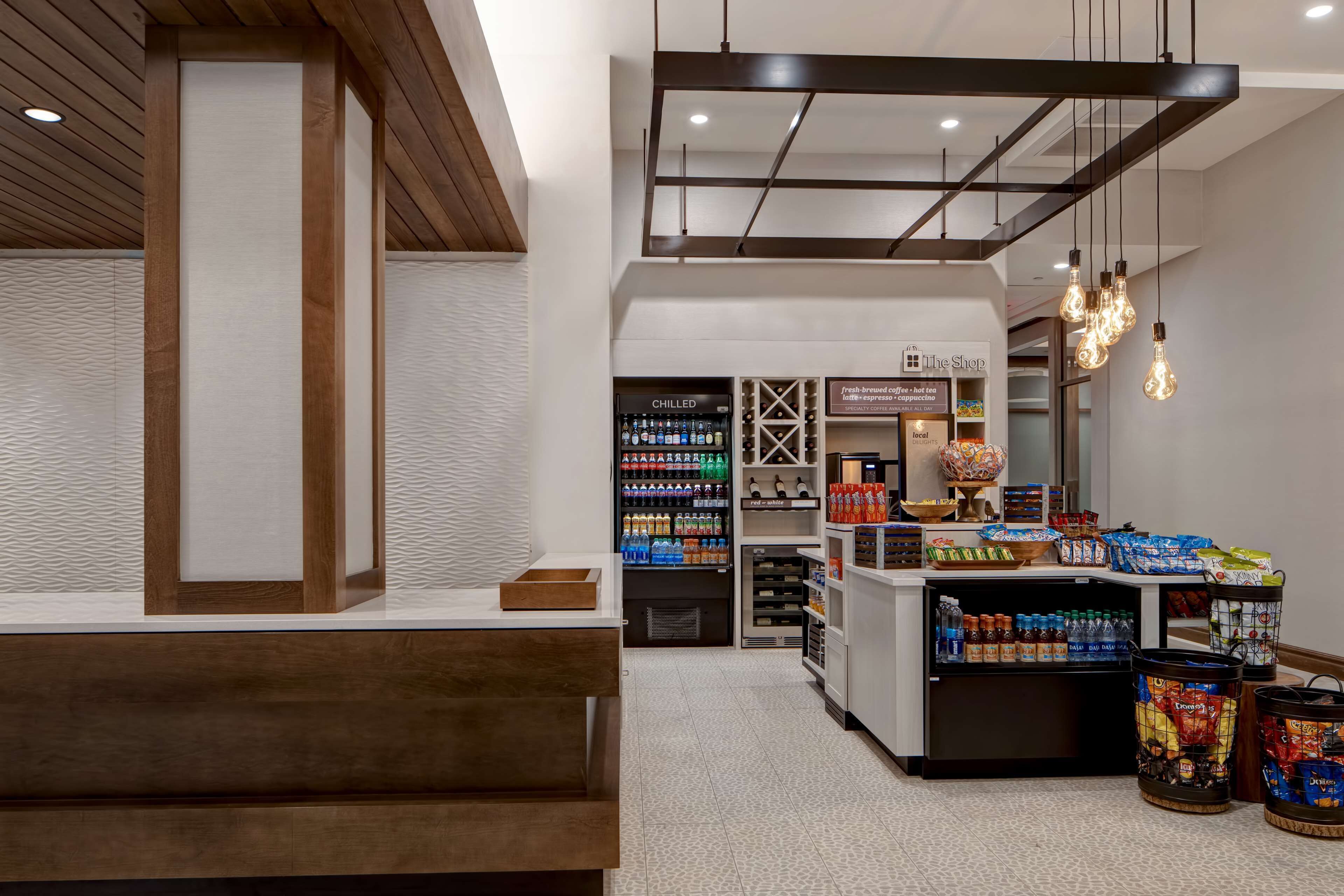 Un moderno vestíbulo de hotel con mostrador de recepción, refrigerador para bebidas y barra de aperitivos.