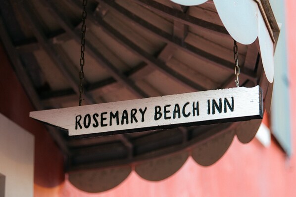 A wooden sign with the text "ROSEMARY BEACH INN" hanging from a chain.