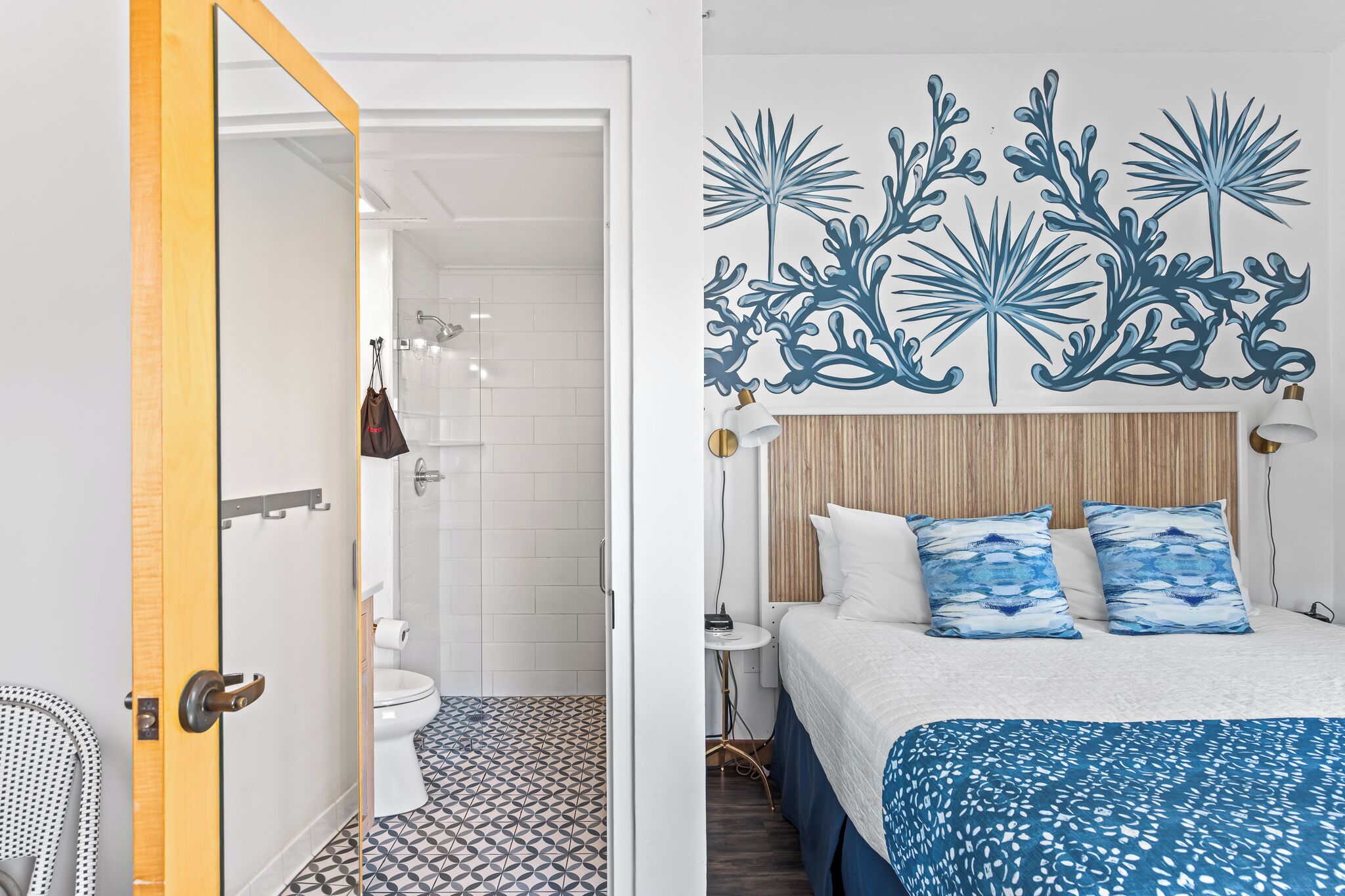 A hotel room with a bed, a nightstand, a wall art piece, and a bathroom with a shower and toilet.