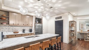 Uma cozinha moderna com ilha de mármore, banquetas de vime, armários de madeira e uma geladeira de aço inoxidável.