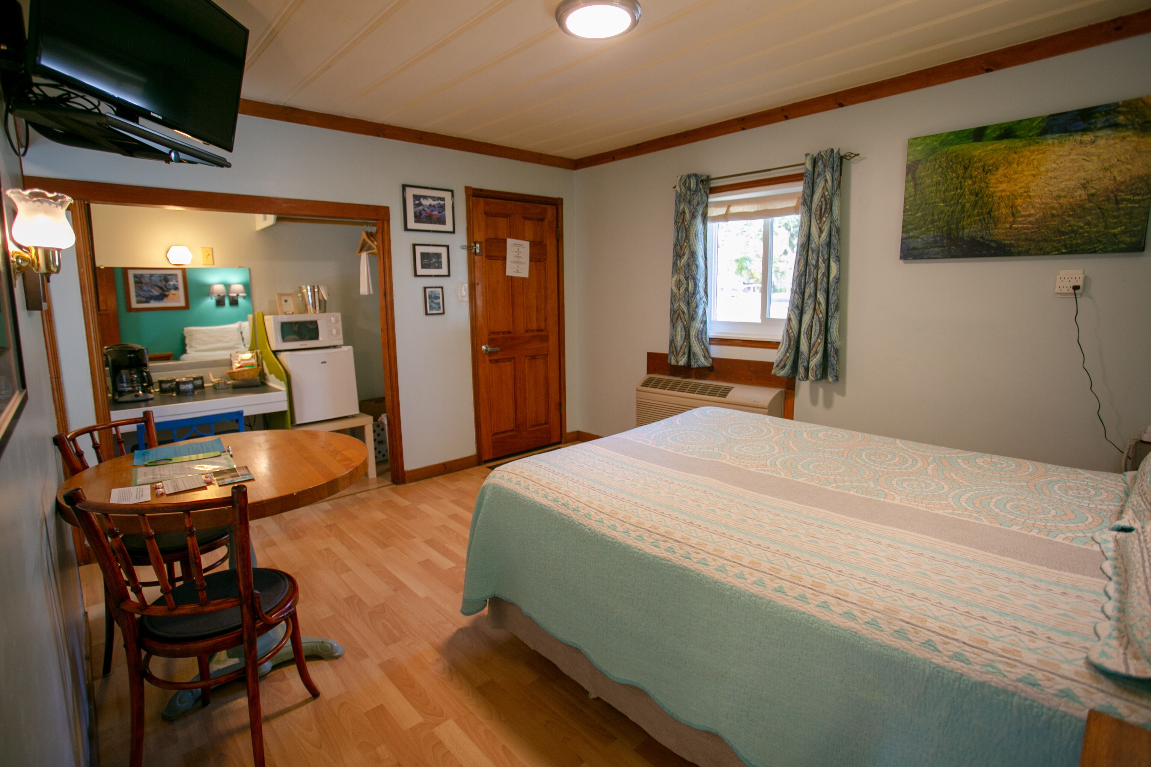 A bedroom with a bed, a desk with a chair, a microwave, a refrigerator, and a television.
