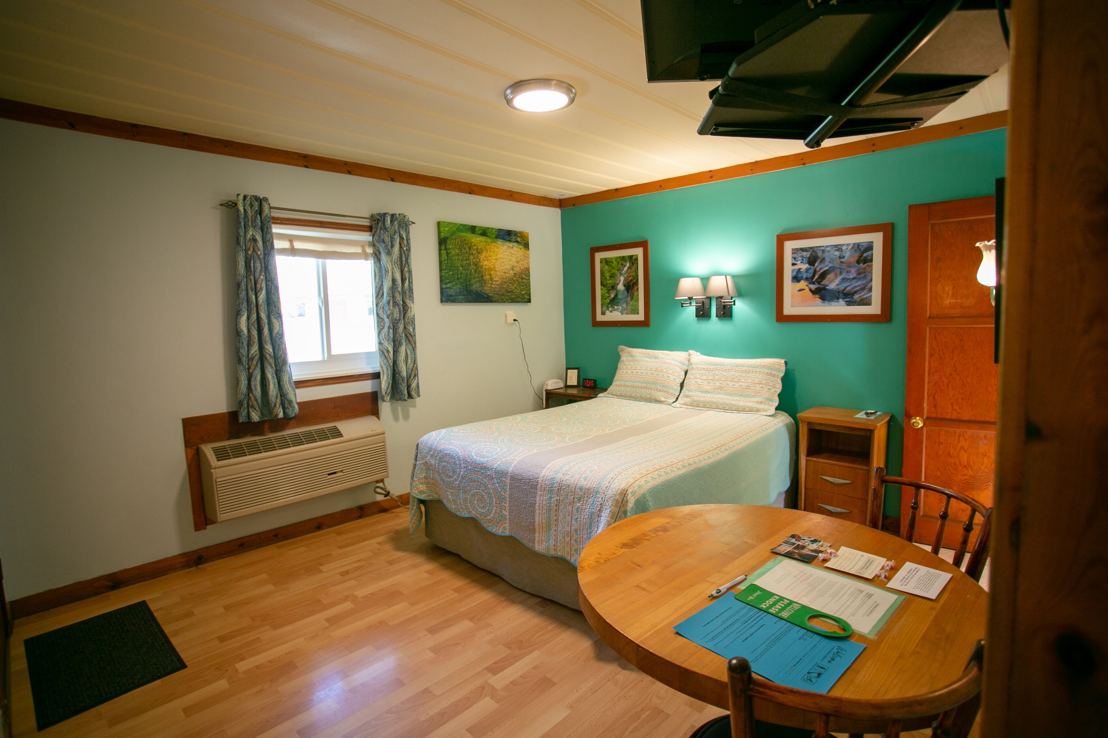 A bedroom with a bed, a wooden table with a chair, a window with curtains, and wall-mounted lamps.