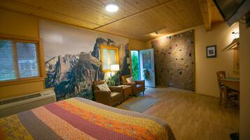 A room with a bed, two chairs, a table, a climbing wall, and a window with blinds.