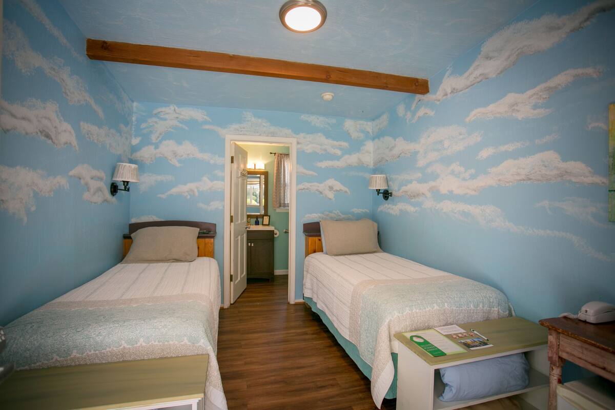 A room with two beds, wooden beams on the ceiling, and a door leading to a bathroom.