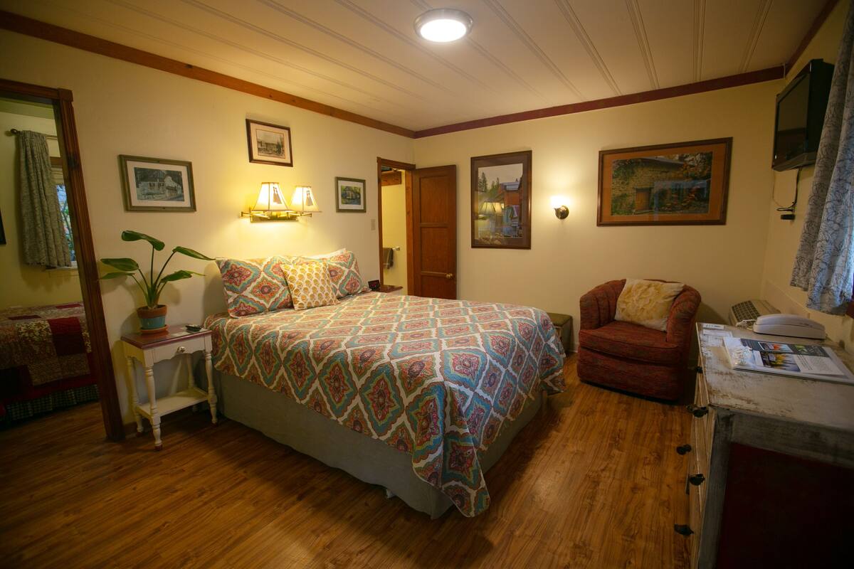 A bedroom with a bed, a chair, a desk, a lamp, and a plant.