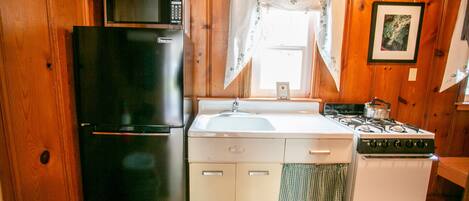 A compact kitchen with a black refrigerator, a white sink, and a stove.