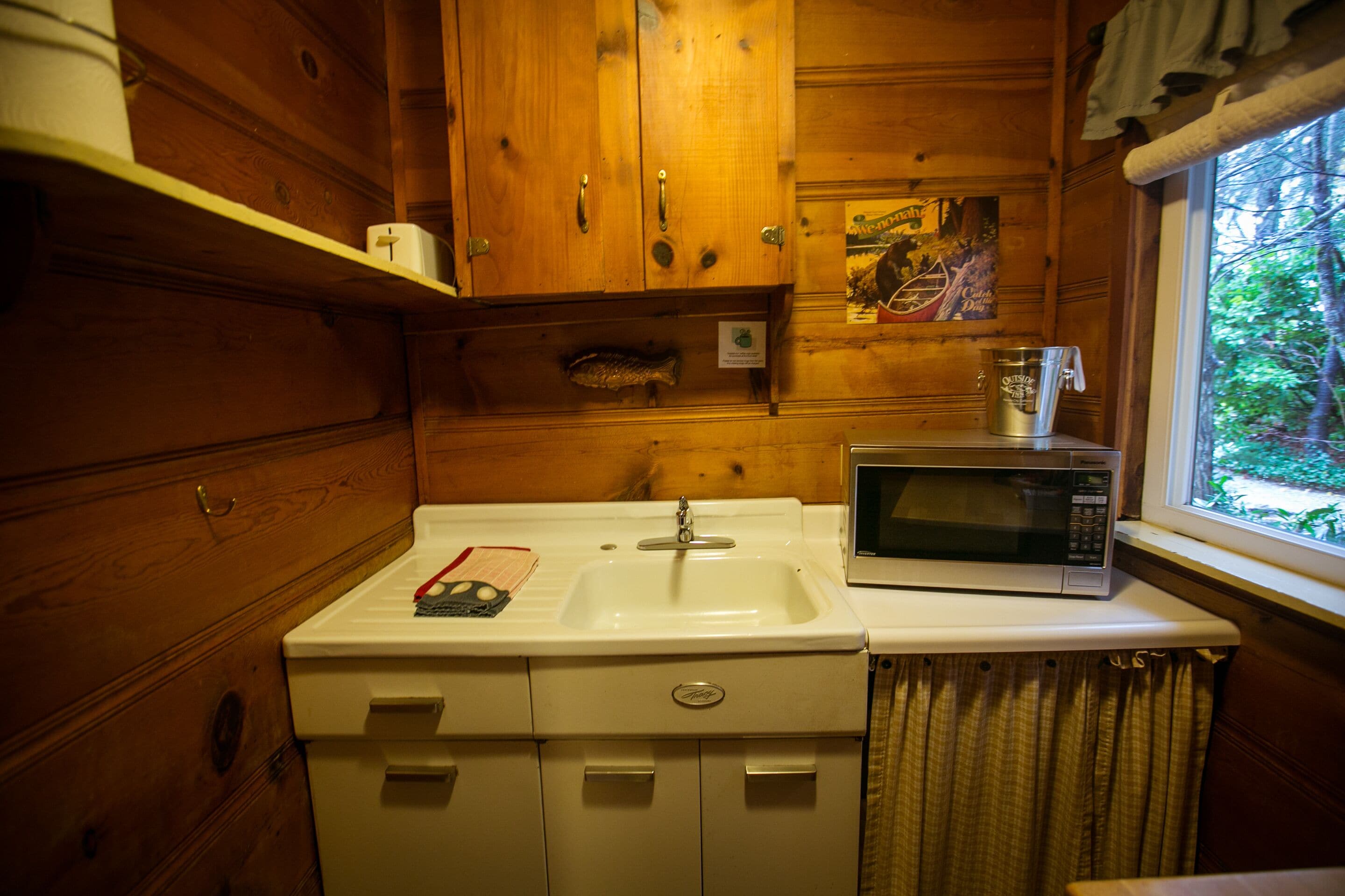 A compact wooden cabin-style kitchen with a white sink, a microwave, and wooden cabinets.