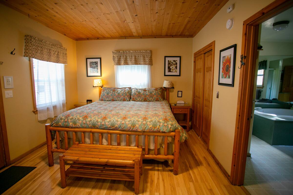 A wooden-framed bed with a floral bedspread, a wooden bench, and a wooden floor.