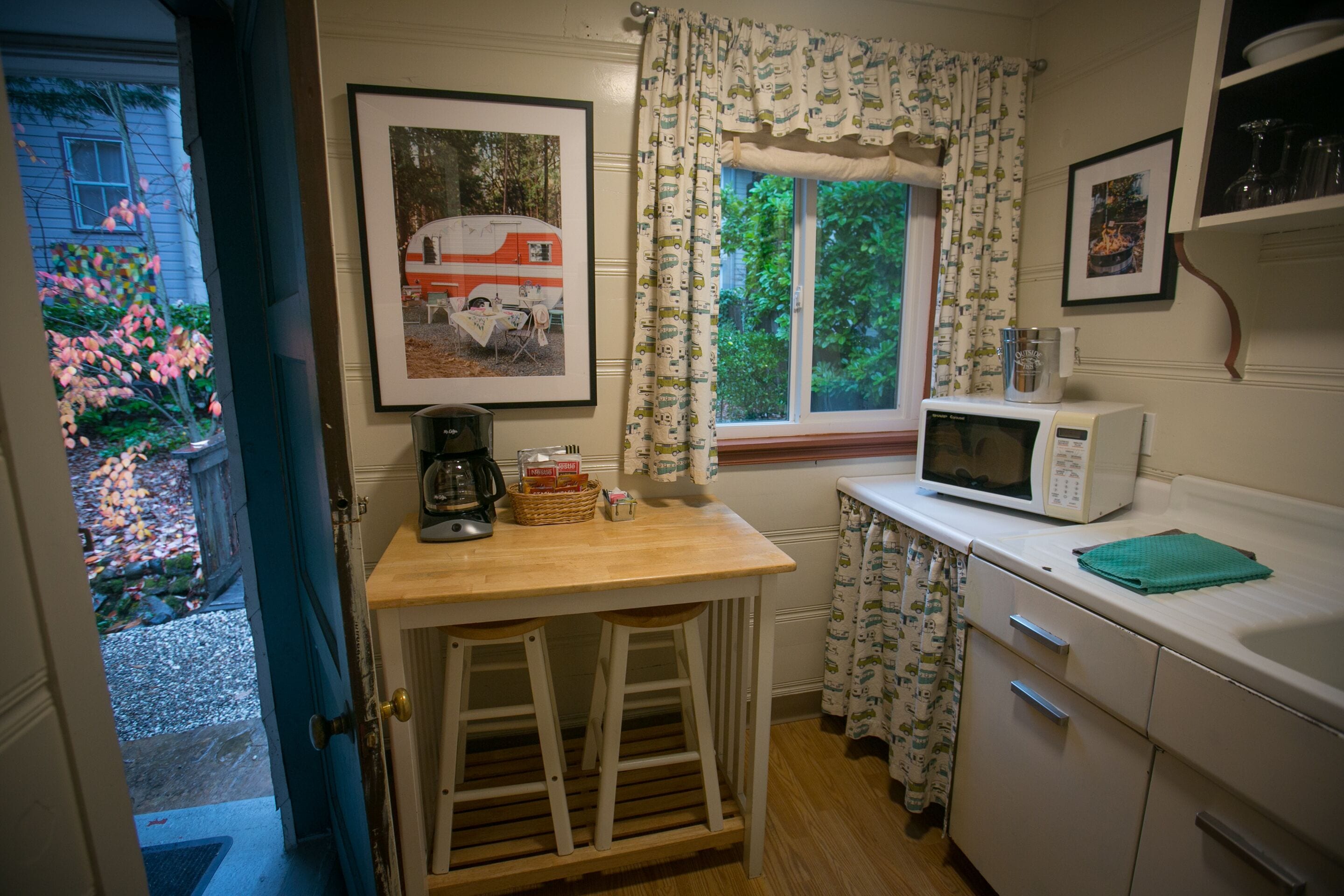 A kitchen with a wooden table, bar stools, a microwave, and a window with curtains.