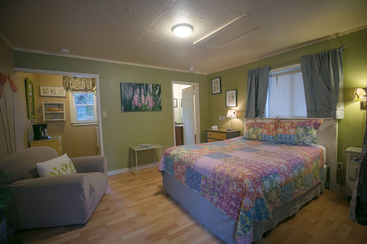 A bedroom with a bed, a chair, a nightstand, and a dresser.