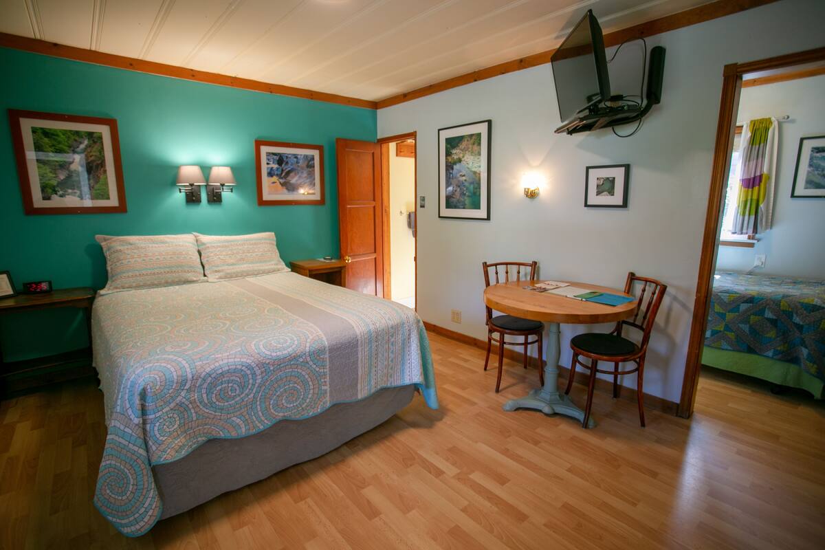 A bedroom with a bed, a wooden dining table with chairs, and a TV mounted on the wall.