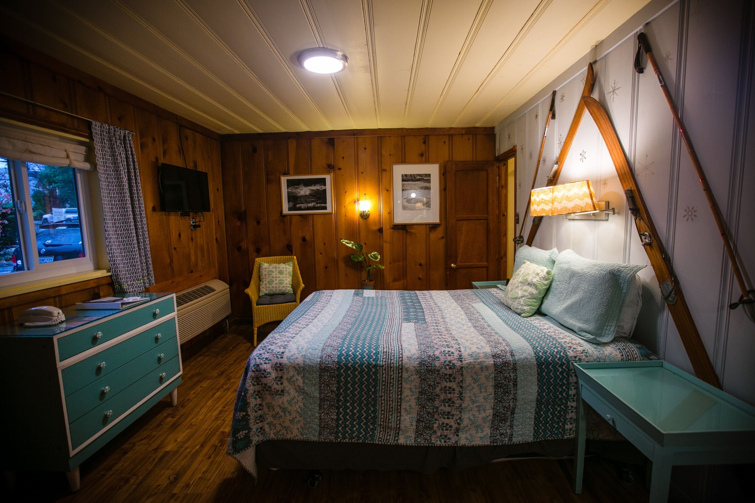 A cozy room with a bed, a dresser, a chair, a lamp, and a window with a view of the outside.