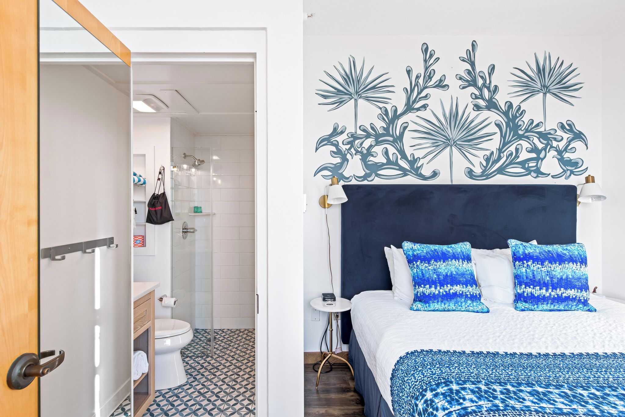 Habitación de hotel con cama, mesita de noche, una obra de arte en la pared y un baño visible a través de una puerta abierta.