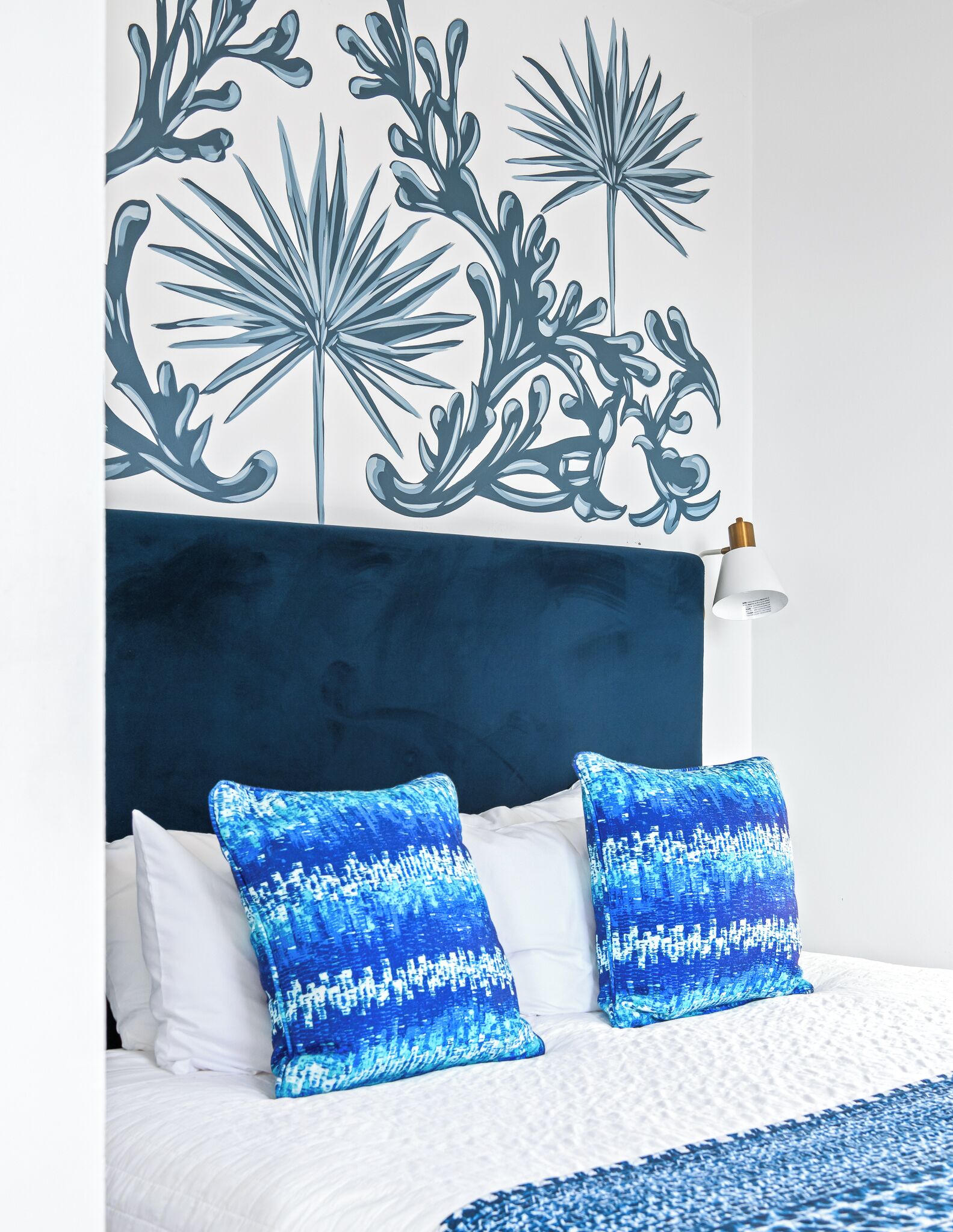 A bedroom with a blue and white color scheme, featuring a bed with white and blue pillows, a blue headboard, and a wall with a blue and white abstract design.
