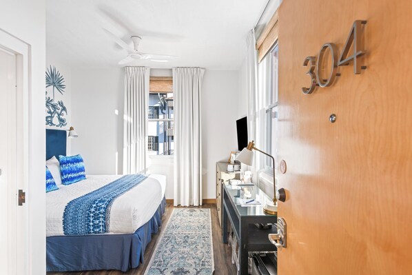 Habitación de hotel con cama, escritorio, televisor y puerta de madera con el número 304.