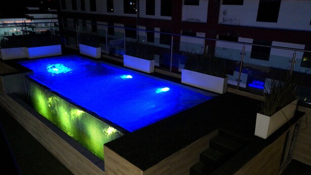 A rectangular pool with blue lighting, surrounded by wooden borders and white planters.