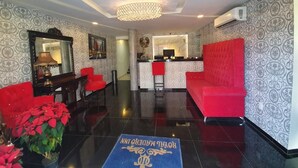 A hotel lobby with a reception desk, red seating, a chandelier, and patterned wallpaper.