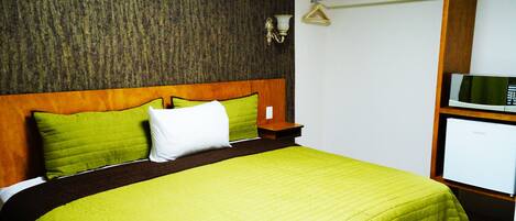 Quarto de hotel com uma cama, mesa de cabeceira, televisão fixada na parede e um cabideiro.
