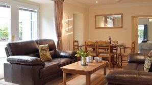 A living room with a brown leather sofa, a wooden coffee table, and a dining area with a wooden table and chairs. - Victoria House - UK13380 (Llansteffan, near Carmarthen)