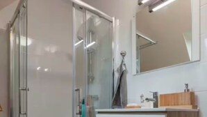 Ein modernes Badezimmer mit einer Duschkabine aus Glas, einem weißen Waschtisch mit Holzplatte und einem Spiegel darüber.