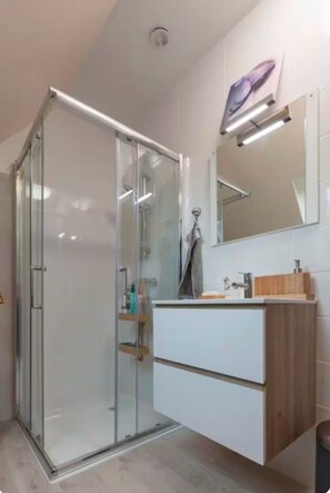 A modern bathroom with a glass shower enclosure, a white vanity with a wooden countertop, and a mirror above the vanity. - Studio Phenix at first floor (Plouédern)