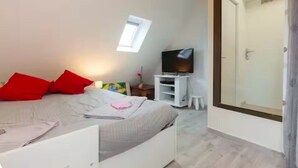 Ein Schlafzimmer mit einem Bett, einem Fernseher, einem kleinen weißen Tisch und einem Fenster.
