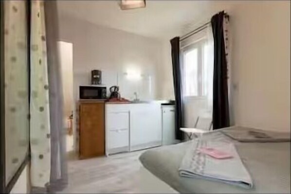A small, compact room with a kitchenette, a bed, and a window with curtains.