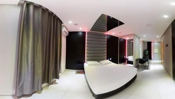 A modern hotel room with a curved bed, a seating area, and a dining table. - Plaza Motel - Adults Only (Votorantim)