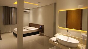 A modern hotel room with a large bed, a built-in vanity with a sink, and a large mirror. - Plaza Motel - Adults Only (Votorantim)
