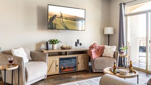 A living room with a fireplace, a television mounted on the wall, and a large window with curtains. - Newly Renovated Sparkling Springs by J and Amy BL990802 (Mesquite)