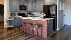 A modern kitchen with blue cabinets, a black refrigerator, and a central island with stools. - Newly Renovated Sparkling Springs by J and Amy BL990802 (Mesquite)