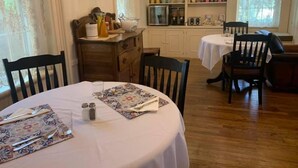 A dining area with a round table set for four, a wooden cabinet, and a kitchen area with shelves stocked with kitchenware. - Willard Richards Inn (Nauvoo)