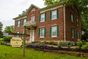 A two-story brick building with green shutters, a balcony, and a sign indicating it is Willard Richards Inn offering bed and breakfast.