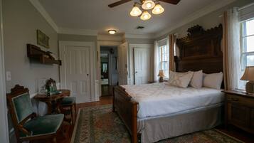 A bedroom with a large bed, a wooden headboard, a ceiling fan, and a small table with chairs.