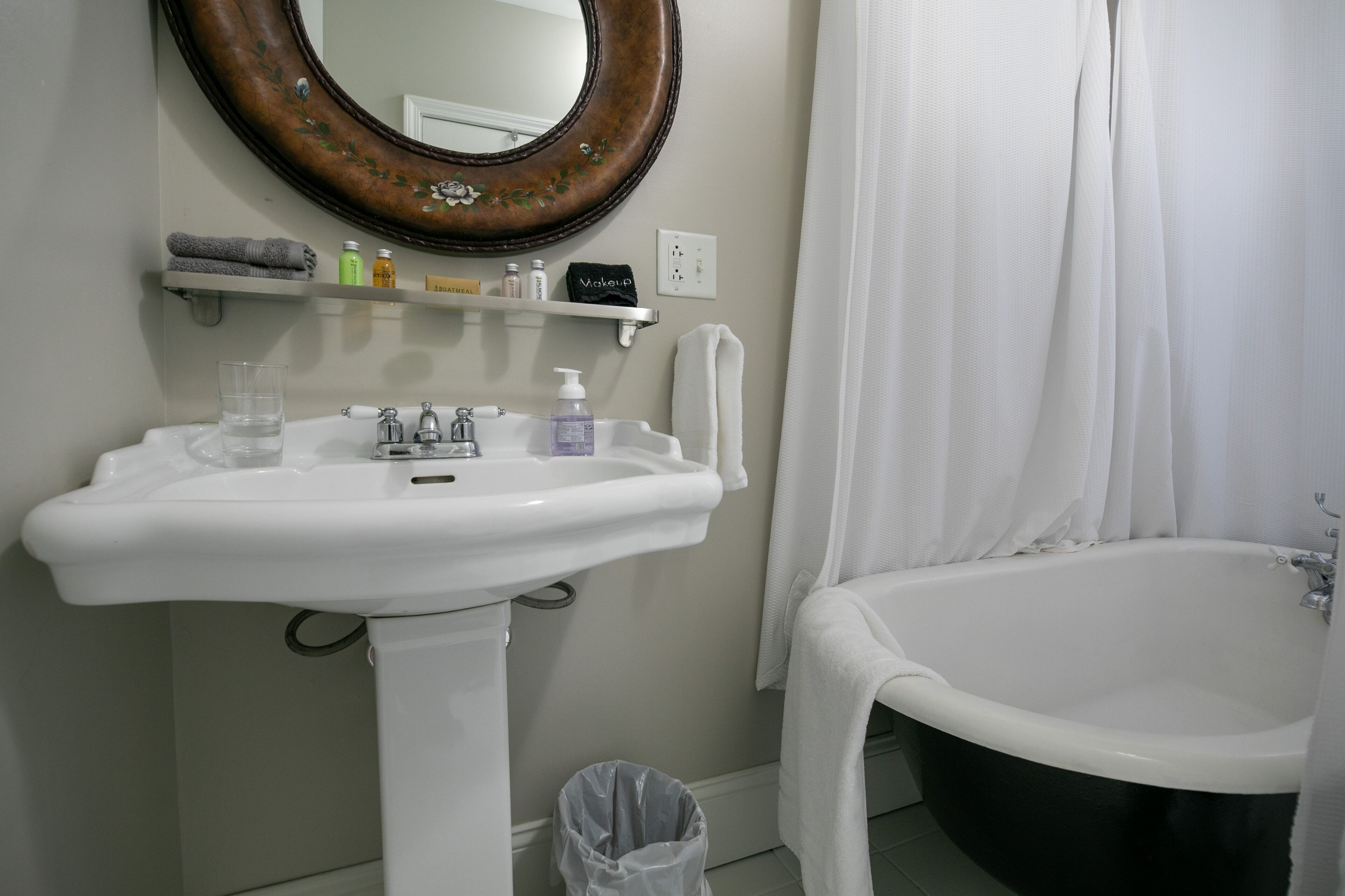 A bathroom with a white sink, a mirror with a floral frame, a bathtub, and a shower curtain.