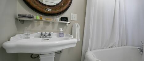 A bathroom with a white sink, a mirror with a floral frame, a bathtub, and a shower curtain.