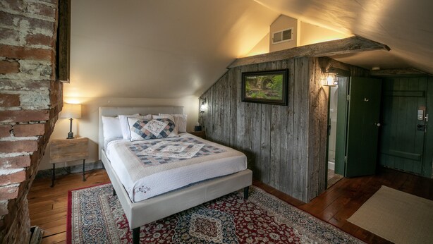 A bedroom with a bed, a wooden headboard, a nightstand, a lamp, a rug, and a door. - Willard Richards Inn (Nauvoo)