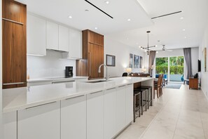 A modern kitchen with white cabinetry, a central island, and a dining area with a view.