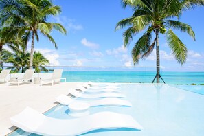Una piscina infinita con sillones blancos y palmeras, con vista a un océano azul y despejado.