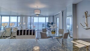 Ett modernt hotellrum med ett stort matbord i glas, en takfläkt och utsikt över havet.