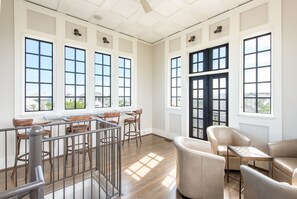 Relax in a spacious room with high ceilings and large windows, featuring a comfortable seating area with leather armchairs and a small table.