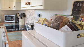 A kitchen with white cabinets, a microwave, a toaster, and a bread basket containing various breads and a jar of jam. - 2 bedroom accommodation in Llansteffan, near Carmarthen (Llansteffan, near Carmarthen)