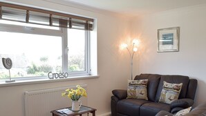 A living room with a brown leather sofa, a small wooden table with a vase of yellow flowers, a radiator, and a window with blinds. - 2 bedroom accommodation in Llansteffan, near Carmarthen (Llansteffan, near Carmarthen)