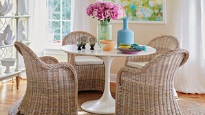 A dining area with wicker chairs, a white table, and a vase of flowers.