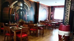 Un restaurant avec des tables et des chaises en bois, une fresque représentant des tonneaux sur le mur, et un grand tonneau au premier plan.