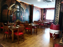 A restaurant with wooden tables and chairs, a mural of barrels on the wall, and a large barrel in the foreground.